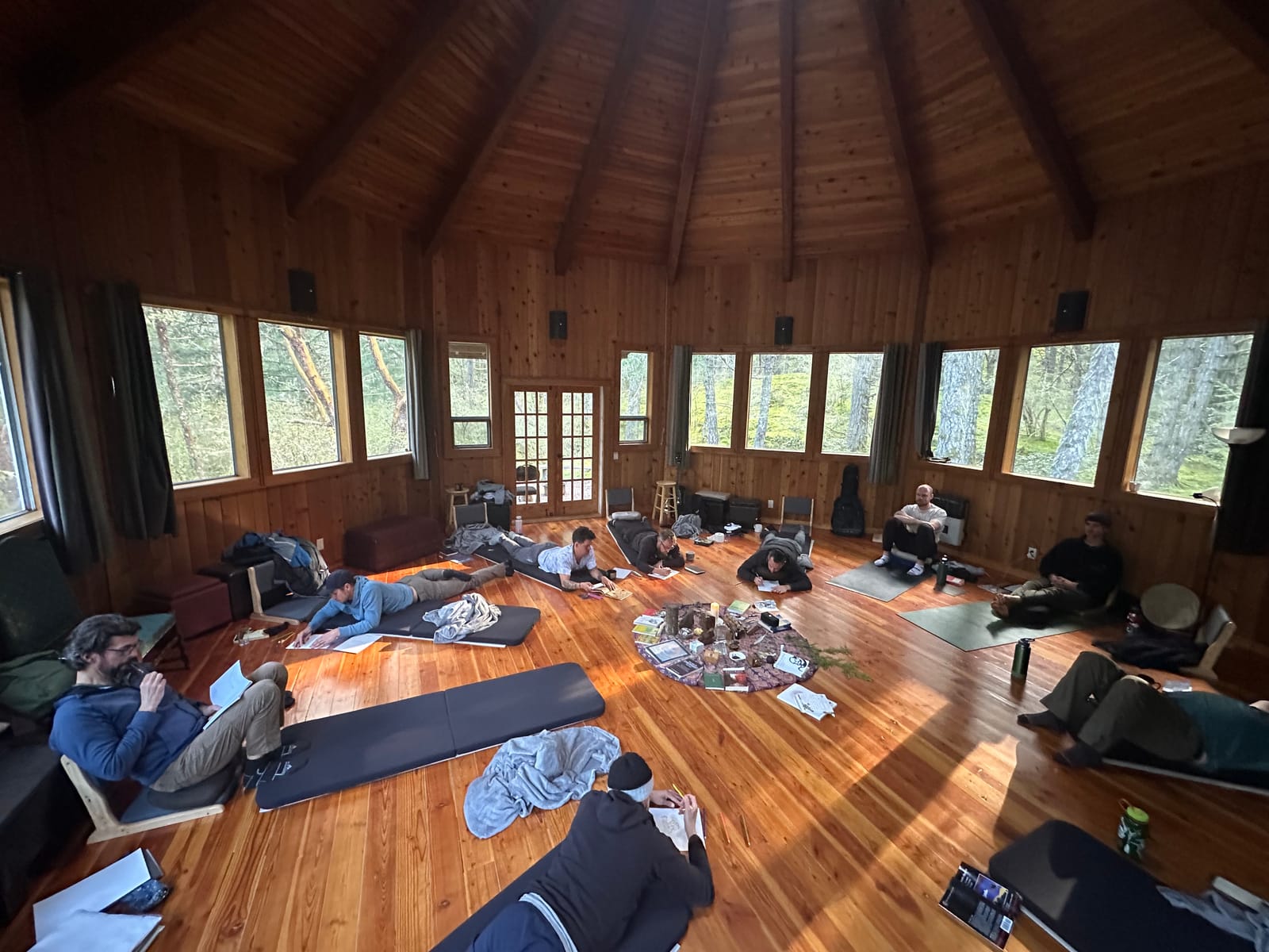 Men journaling on mats around an altar in a wooden hall